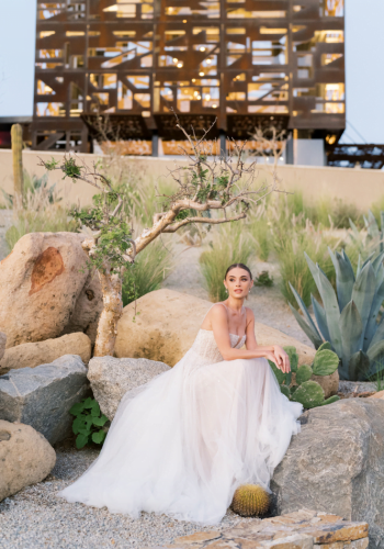 Bride in elegant white gown seated on rocks in garden
