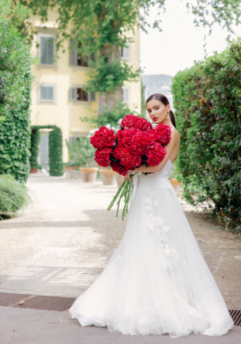 Bride holding large bouquet of red flowers in elegant garden setting