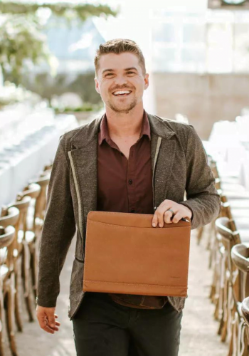 Smiling man walking outside holding a tan leather portfolio